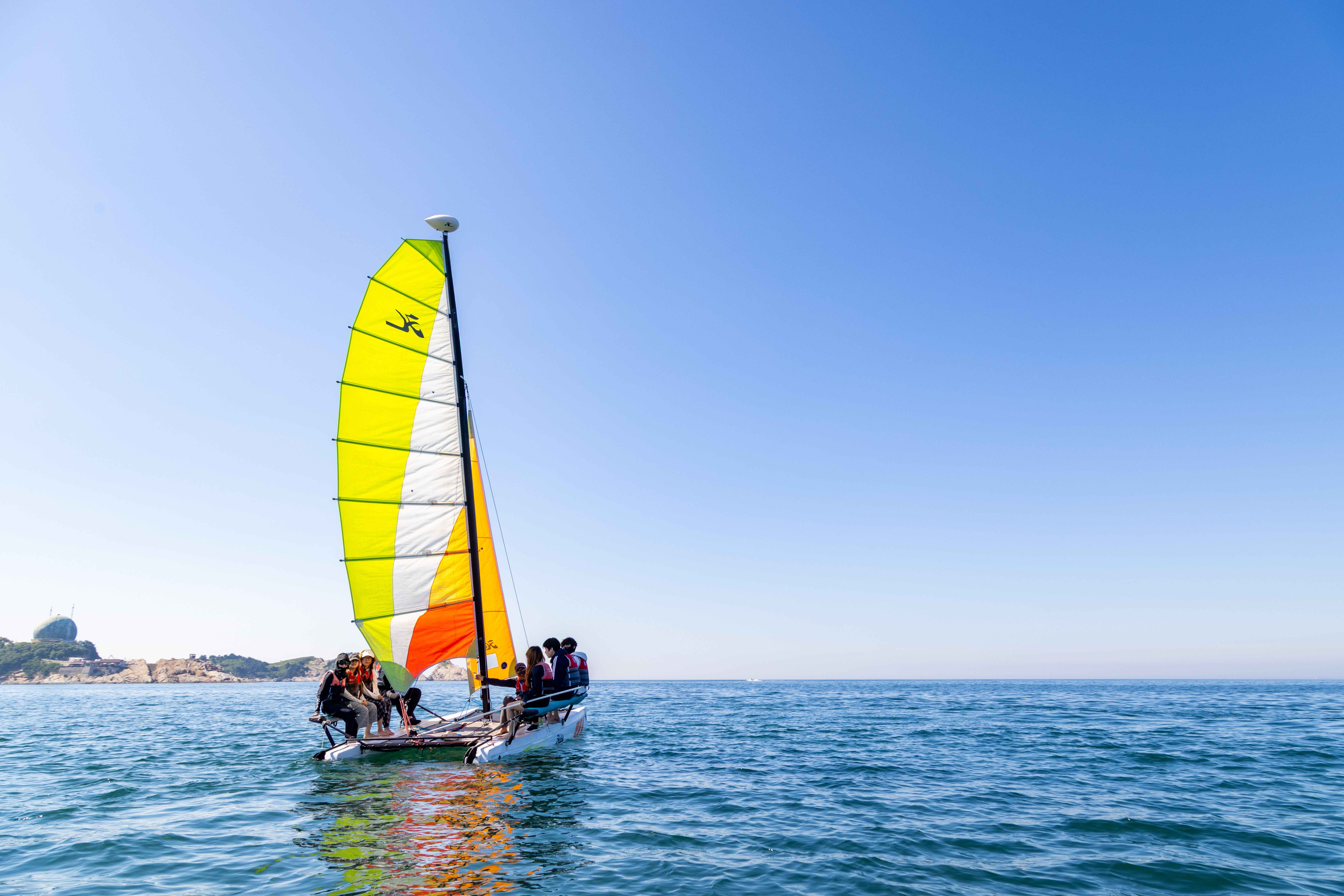 A group enjoys sailing on a colorful sailboat in clear blue waters under a sunny sky.