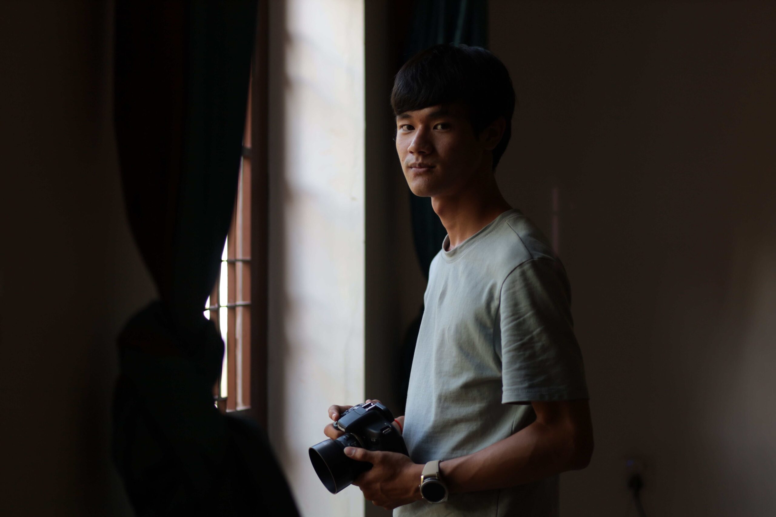 Portrait of an Asian man holding a camera by a window in Phnom Penh, Cambodia.