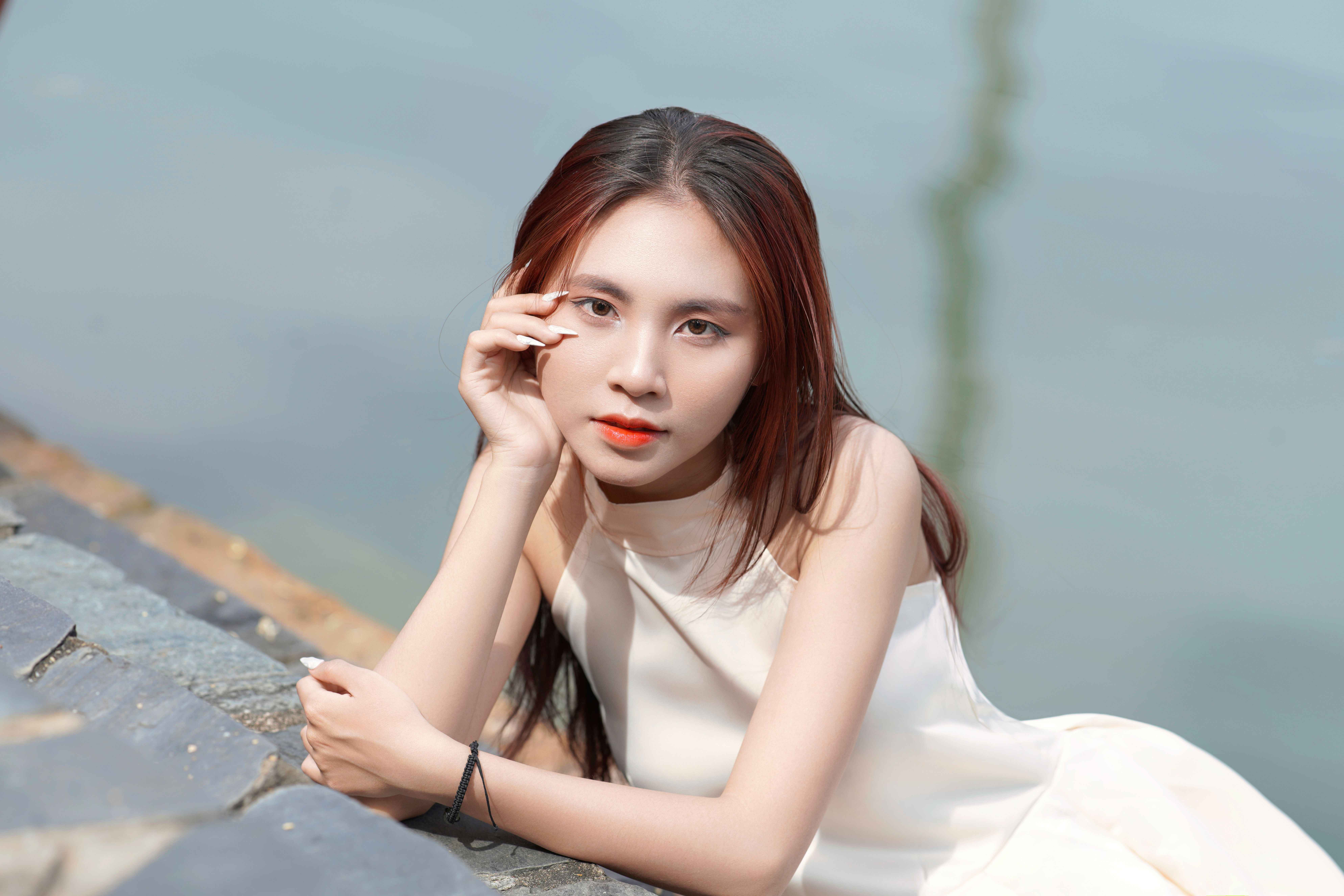 A serene portrait of a young woman in a white dress leaning by the water, exuding elegance and calm.