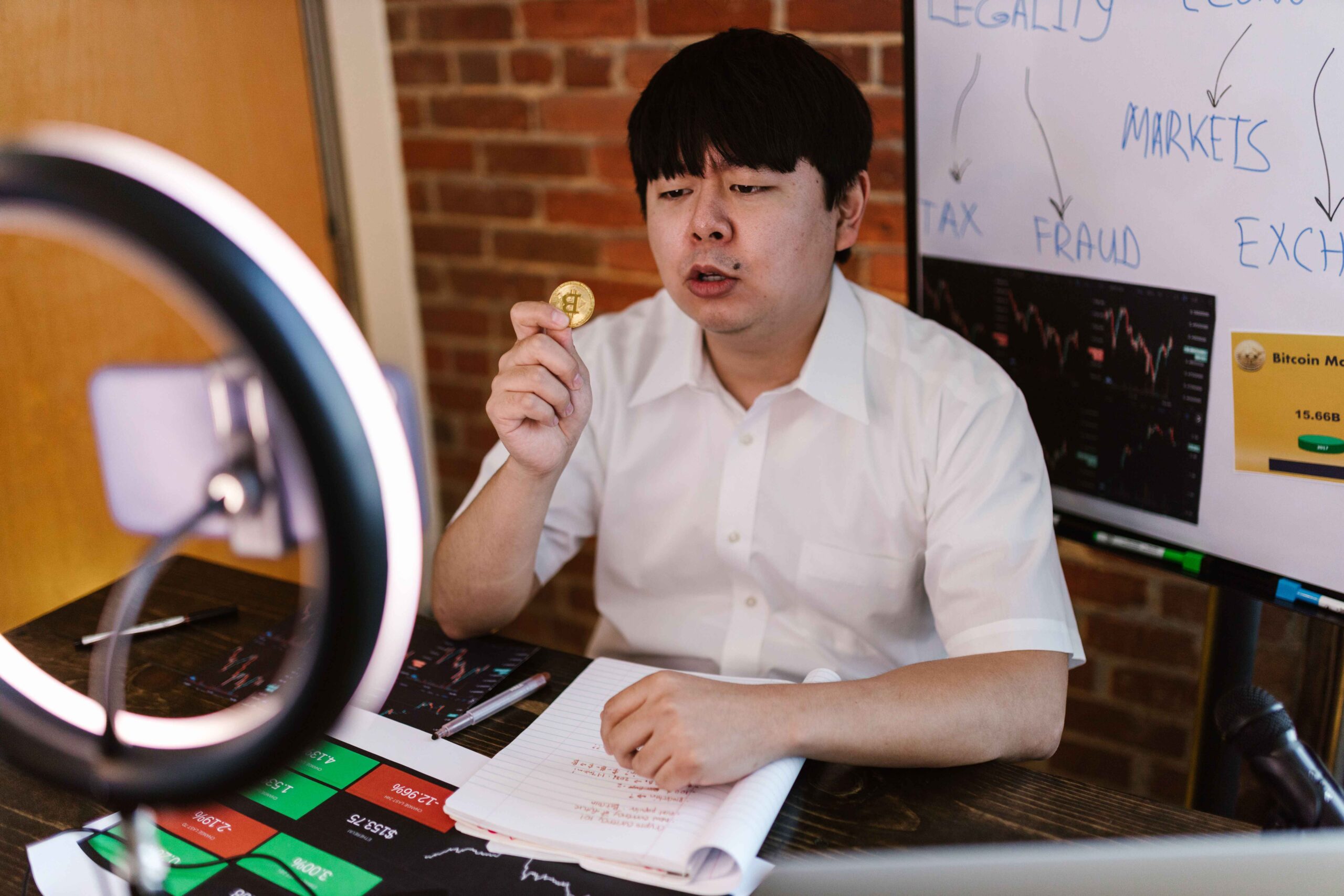 A man using a ring light and recording video about cryptocurrency markets and investments.